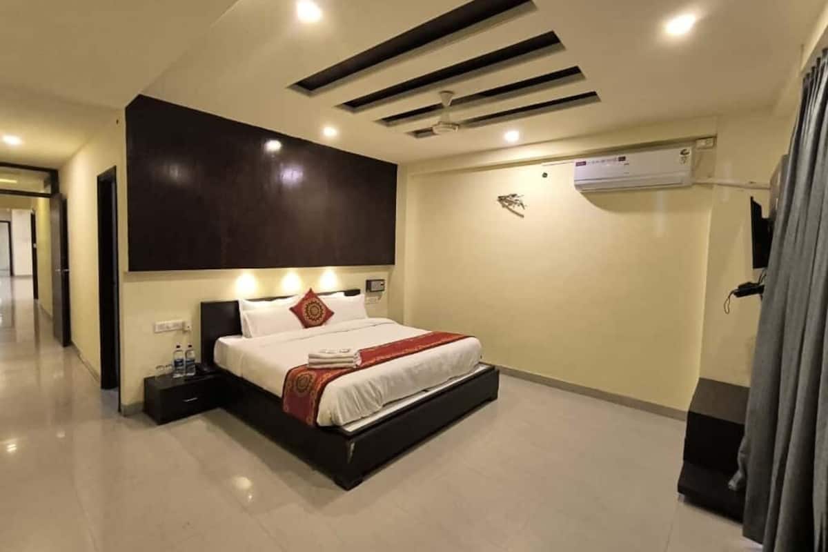 A modern hotel room with a large bed, a dark headboard, recessed ceiling lights, and an air conditioning unit on the wall.