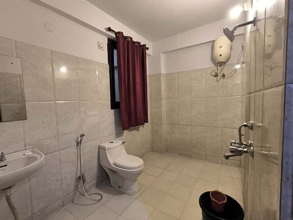 A bathroom with a toilet, sink, shower, and a bucket. - Hotel Shreenathji Inn (Udaipur)