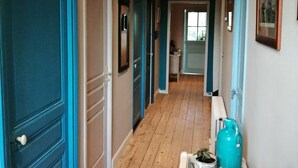 Un pasillo con suelo de madera, puertas color turquesa y un expositor de vidrio con objetos decorativos.