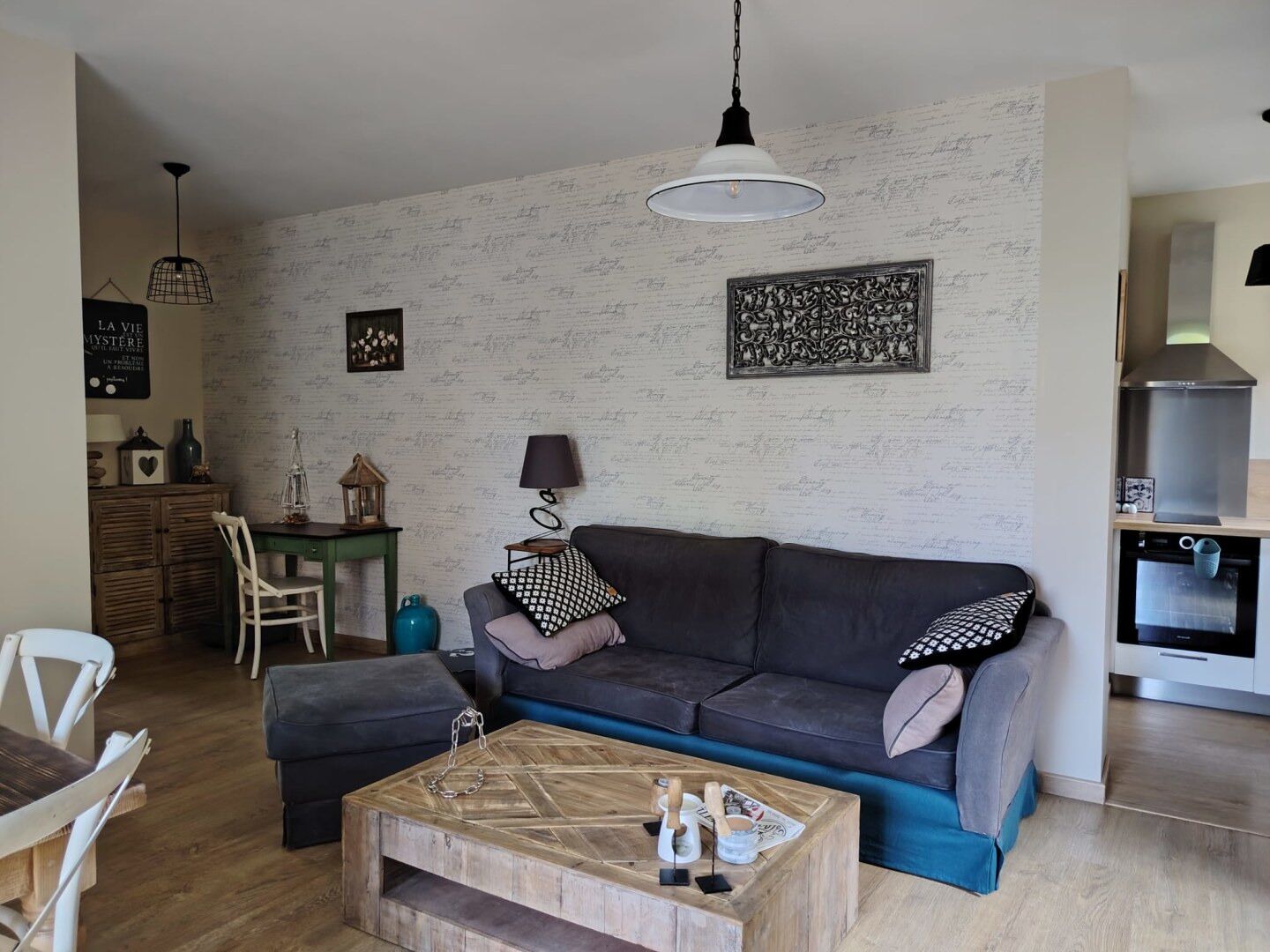 Una sala de estar acogedora con un sofá gris oscuro, una mesa de centro de madera y una lámpara colgante.