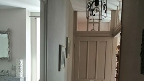 Un pasillo con piso de madera, una puerta blanca que dice 'WC' y una lámpara colgante.
