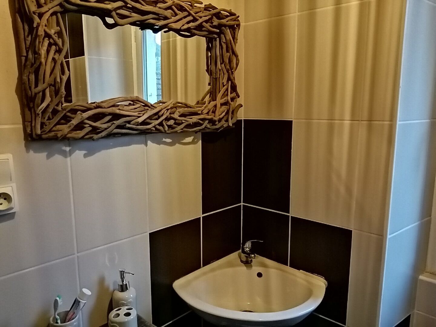 A bathroom with a white sink, a decorative woven mirror frame, and a bottle of hand soap.