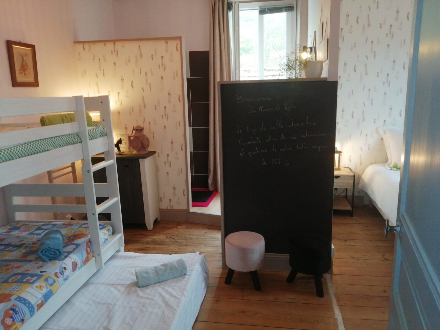A room with bunk beds, a small desk, a chalkboard with a message, and a window with curtains.