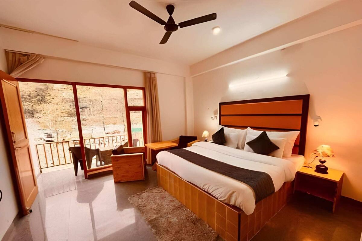 Une chambre à coucher comprenant un lit, un bureau, une chaise, un ventilateur de plafond et une vue dégagée sur l’extérieur grâce à une grande fenêtre.