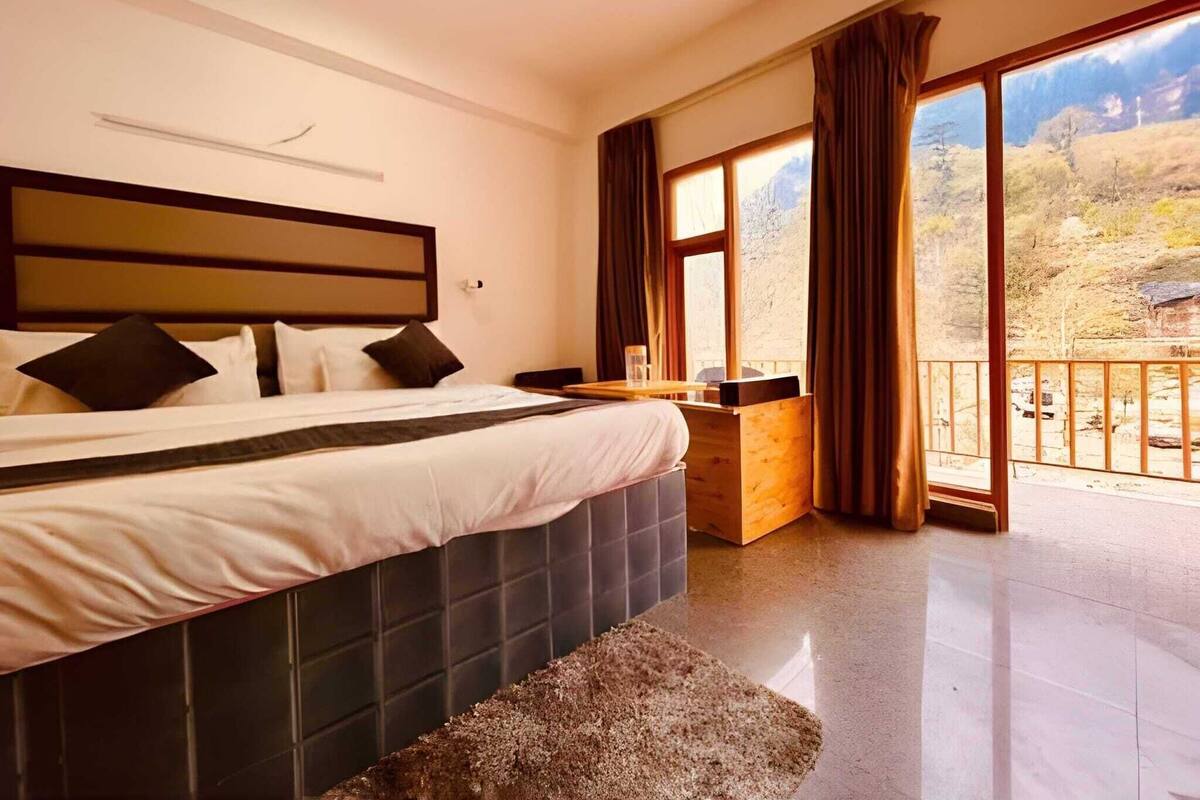 Une chambre à coucher avec un grand lit, une table de chevet en bois et une vue sur un paysage montagneux par une grande fenêtre.