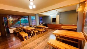 L’intérieur d’un restaurant avec des tables et des bancs en bois, de grandes fenêtres et un luminaire au plafond.
