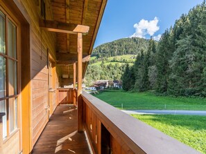 Una cabaña de madera con balcón que da a un valle verde y colinas boscosas.