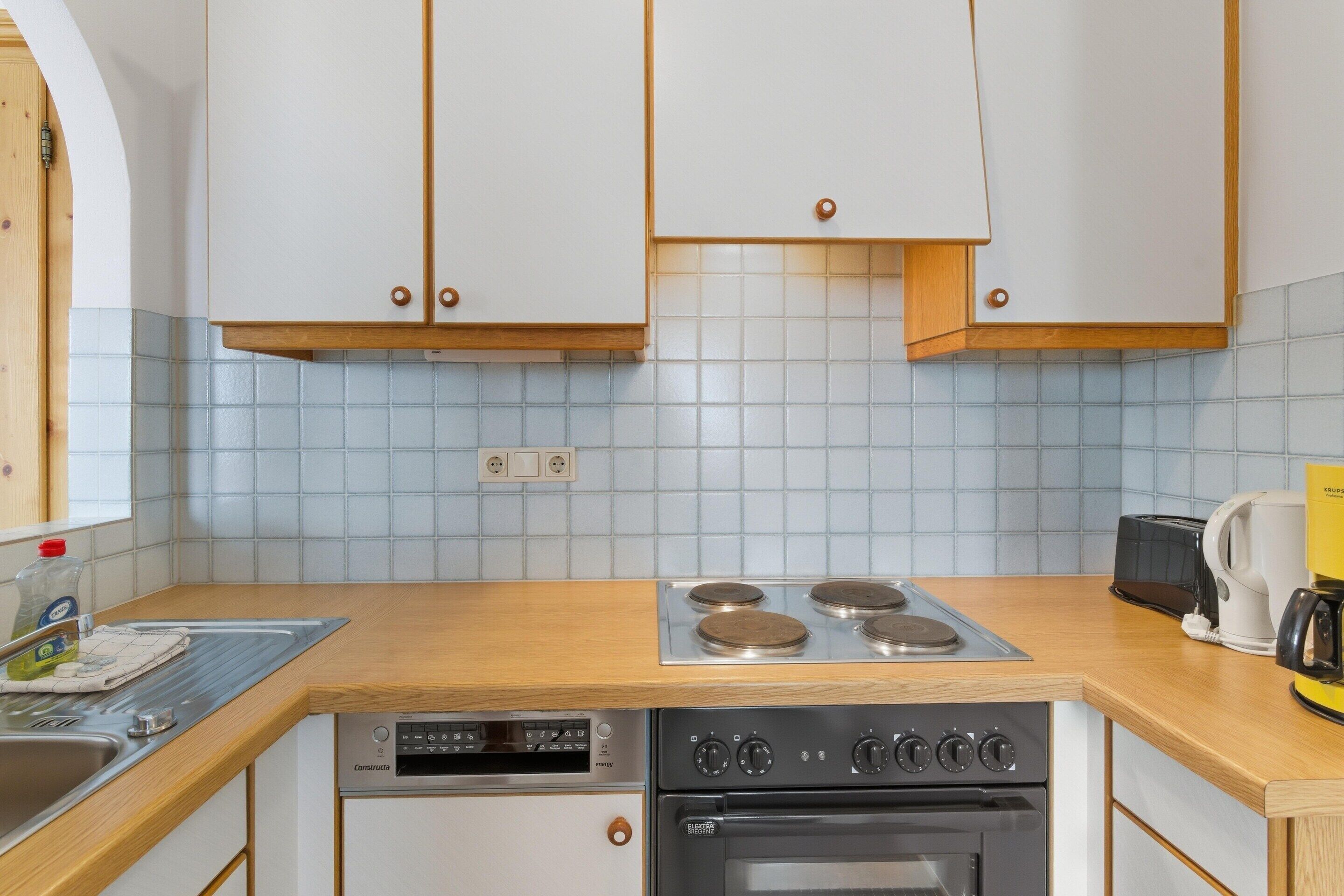 A kitchen with white cabinets, a wooden countertop, a dishwasher, an oven, and a coffee maker.
