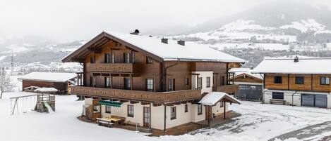 A multi-story wooden building with a balcony, surrounded by snow-covered ground and mountains in the background.