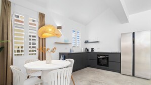 A modern kitchen with a dining area, featuring a round table with chairs, a hanging light fixture, and a built-in oven.