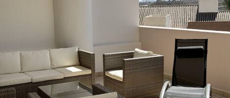 A patio area with wicker furniture, a glass table, and a door.