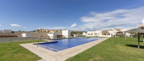 A swimming pool with a clear blue sky and a grassy area.