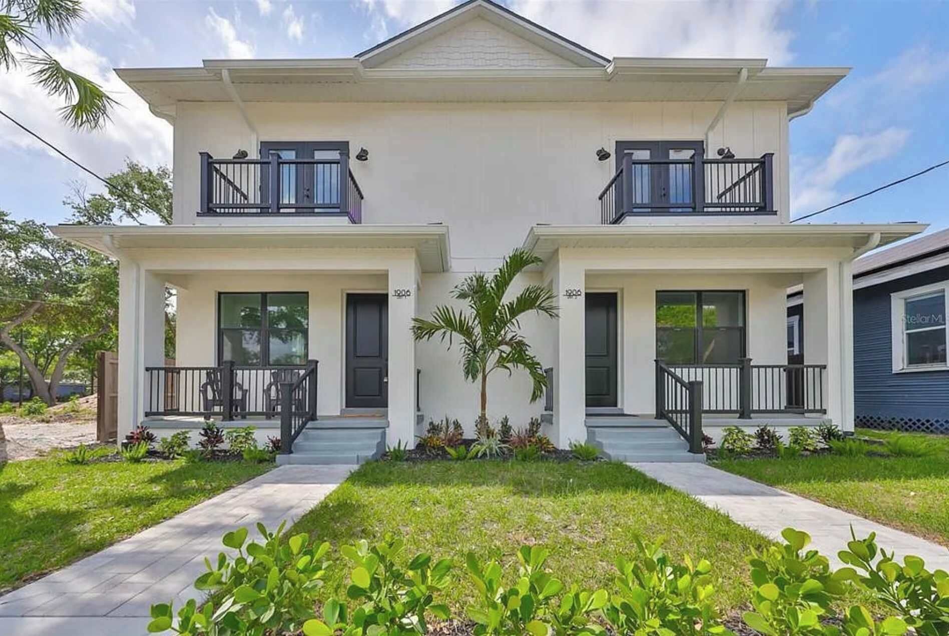 Ein zweistöckiges Haus mit einer Veranda, einem kleinen Garten und blauem Himmel.
