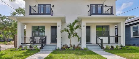 A two-story house with a front porch, a small garden, and a clear sky.