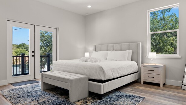 A bedroom with a large bed, a nightstand, a bench, a window with a view, and a door leading to an outdoor area. - NEW Casa Cereza - Stunning New Build In Old Tampa (Tampa)