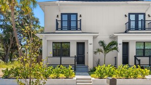 A two-story house with a white exterior, black front door, and windows. There are steps leading to the front door, and a small porch area with a railing. - NEW Casa Cereza - Stunning New Build In Old Tampa (Tampa)