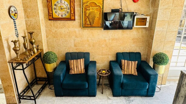 Un vestíbulo con dos sillones azules, un reloj de pared, un cuadro enmarcado y una pequeña mesa con una planta.