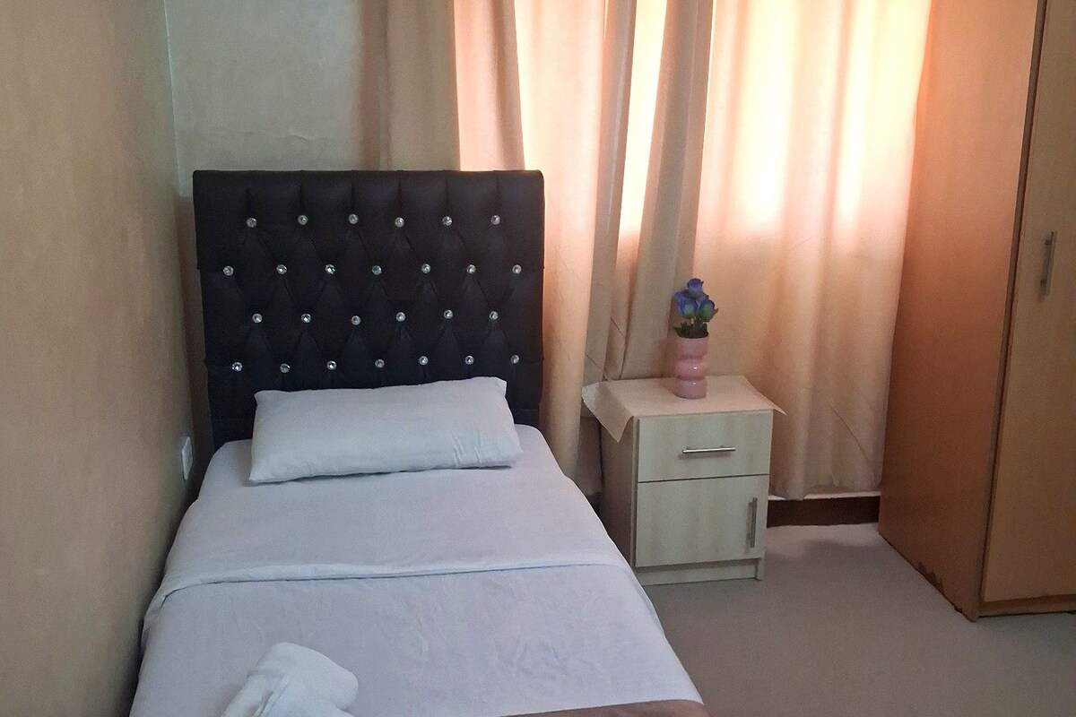 A neatly made bed with a headboard, a bedside table with a vase, and a wardrobe.
