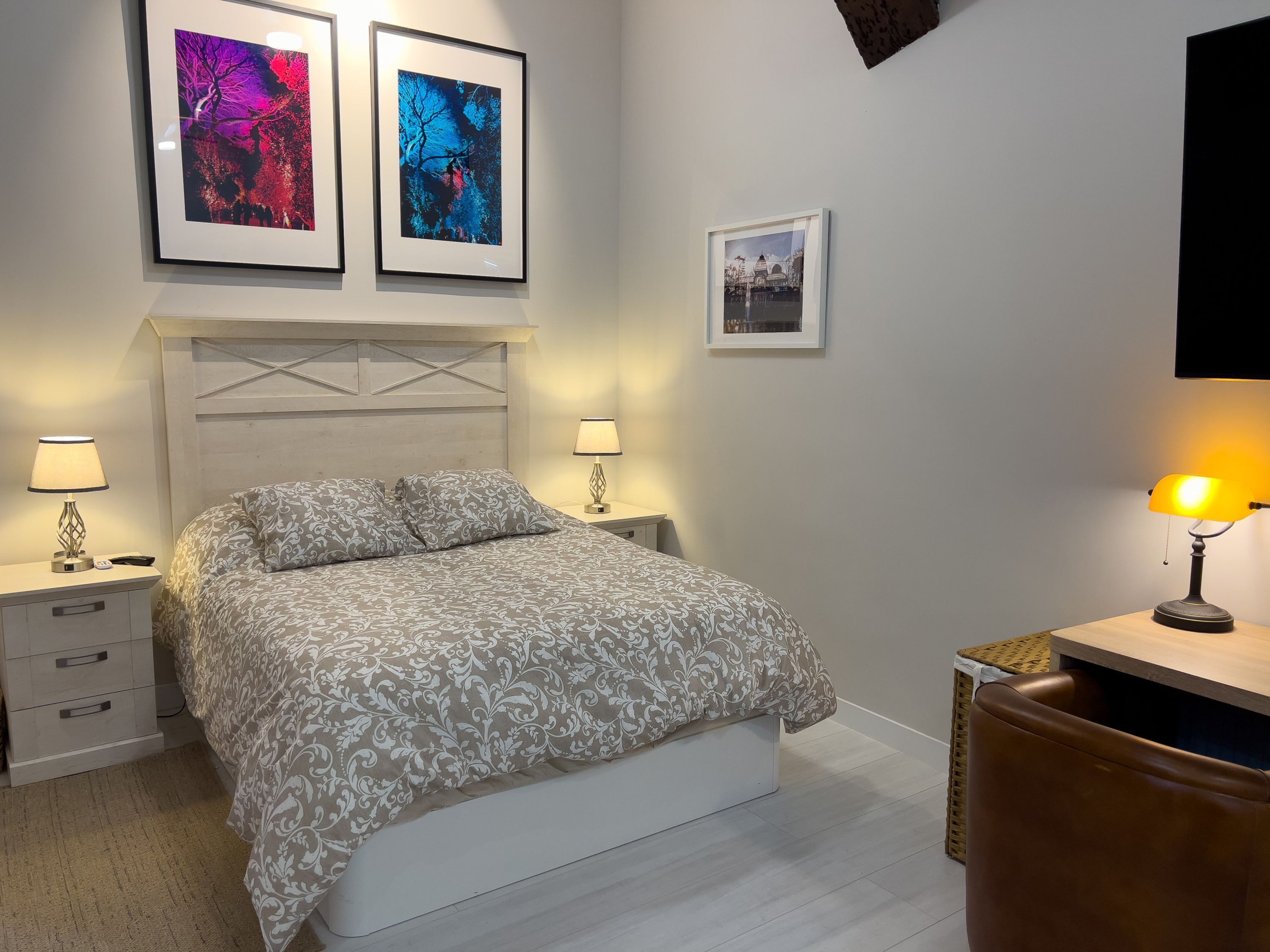 Ein Schlafzimmer mit einem Bett, zwei Nachttischen, einem Schreibtisch mit Stuhl und gerahmten Bildern an der Wand.