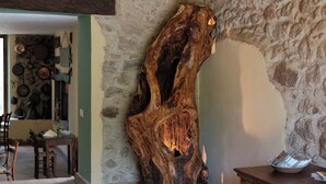 Un intérieur rustique avec un mur en pierre, une sculpture en bois, un coin repas avec des chaises et une table, et un tapis à motifs.