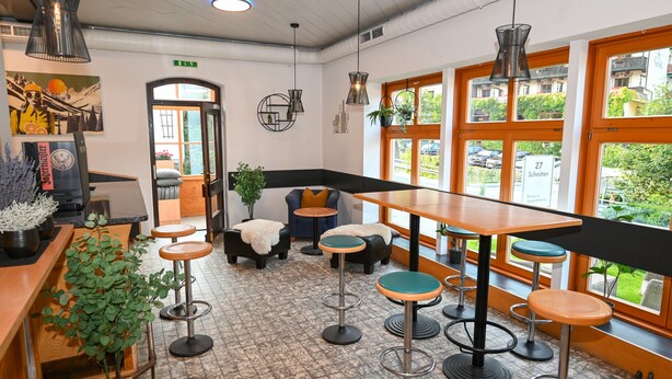 Et moderne interiør med barområde, siddepladser og store vinduer der giver udsigt til gaden.