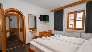 Et hotelværelse med to senge, et fjernsyn ophængt på væggen, en trækommode, et skrivebord med stol og et vindue med gardiner.