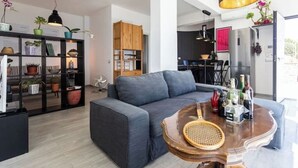 A modern living room with a grey sofa, a wooden coffee table, and a bookshelf filled with plants and books.