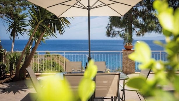An outdoor patio with a table and chairs, a large umbrella, and a view of the ocean.