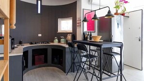 A modern kitchen with a curved island, black bar stools, pendant lighting, and a window.