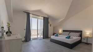 Une chambre à coucher comprenant un lit, des tables de chevet, une commode et une porte-fenêtre coulissante donnant sur un balcon.