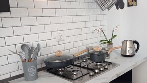 Une cuisine avec un dosseret de carrelage blanc, une cuisinière à gaz, des casseroles, une bouilloire et un porte-ustensiles.