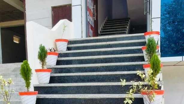 Un escalier extérieur menant à l’entrée d’un bâtiment, avec des plantes en pot disposées à intervalles réguliers.