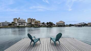 A wooden deck with two chairs facing a calm body of water, with buildings in the background.
