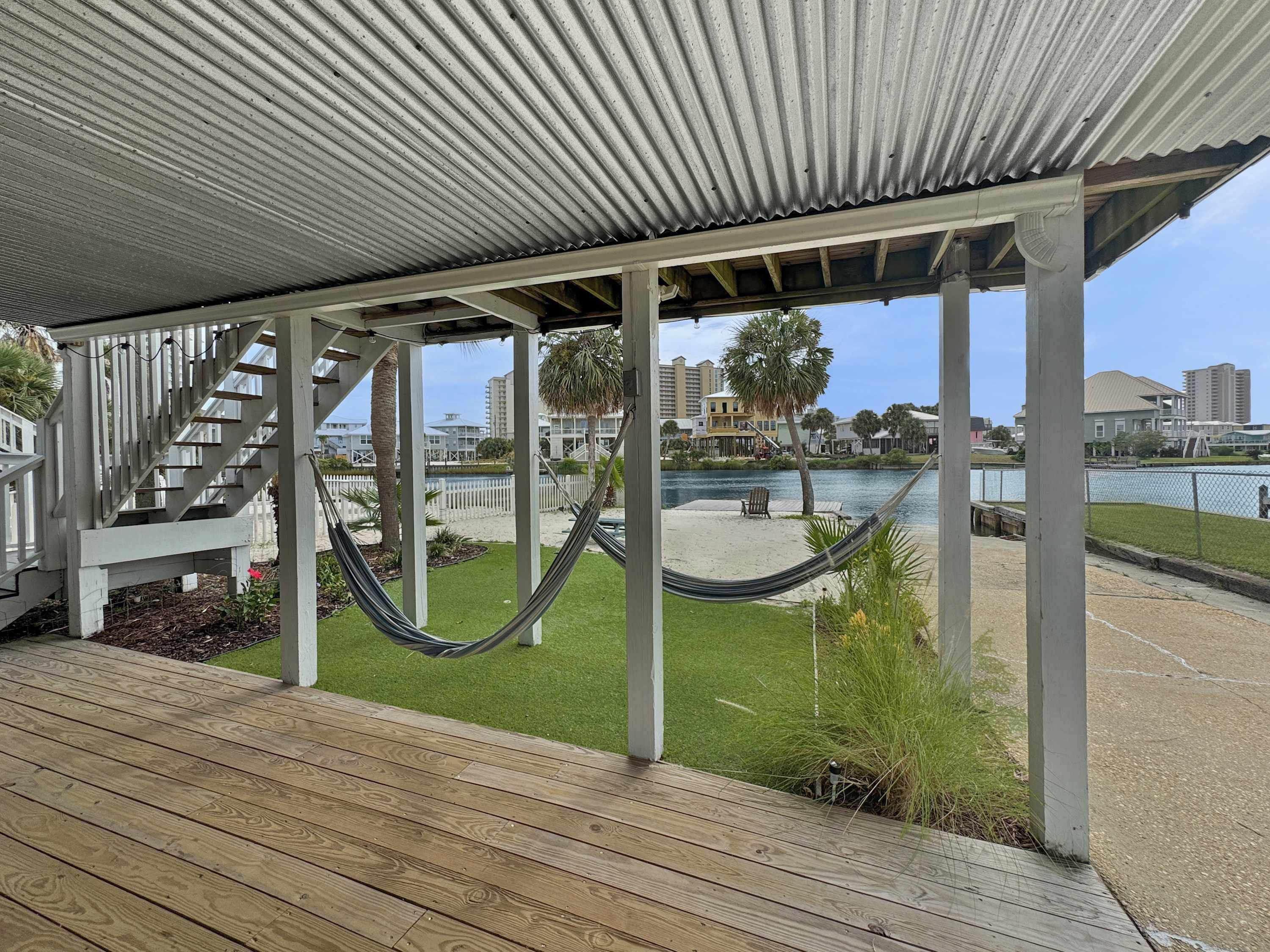 A covered outdoor area with a wooden deck, a hammock, and a view of a waterfront with buildings in the background.