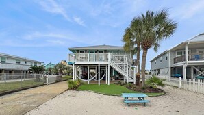 Une propriété située en bord de mer, comprenant un bâtiment à deux étages, un patio couvert et une zone sablonne avec une table de pique-nique.