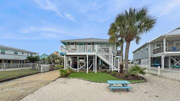 A beachfront property with a two-story building, a covered patio, and a sandy area with a picnic table.