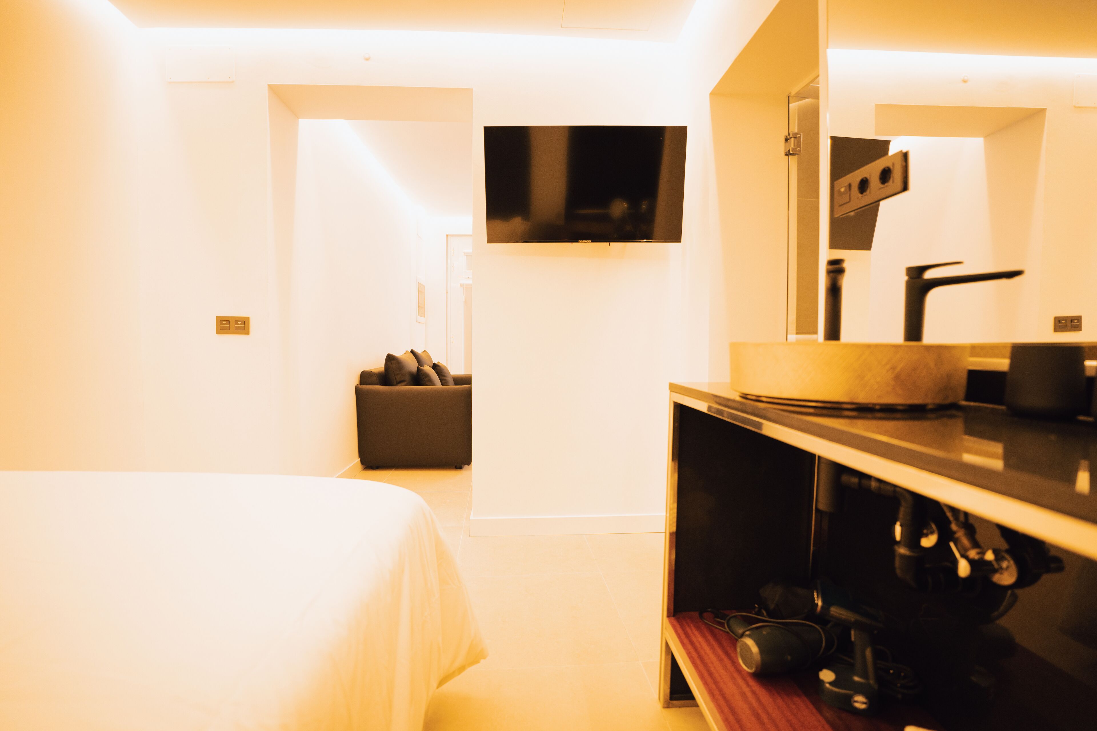 A hotel room with a bed, a TV mounted on the wall, a sofa, and a mirror.