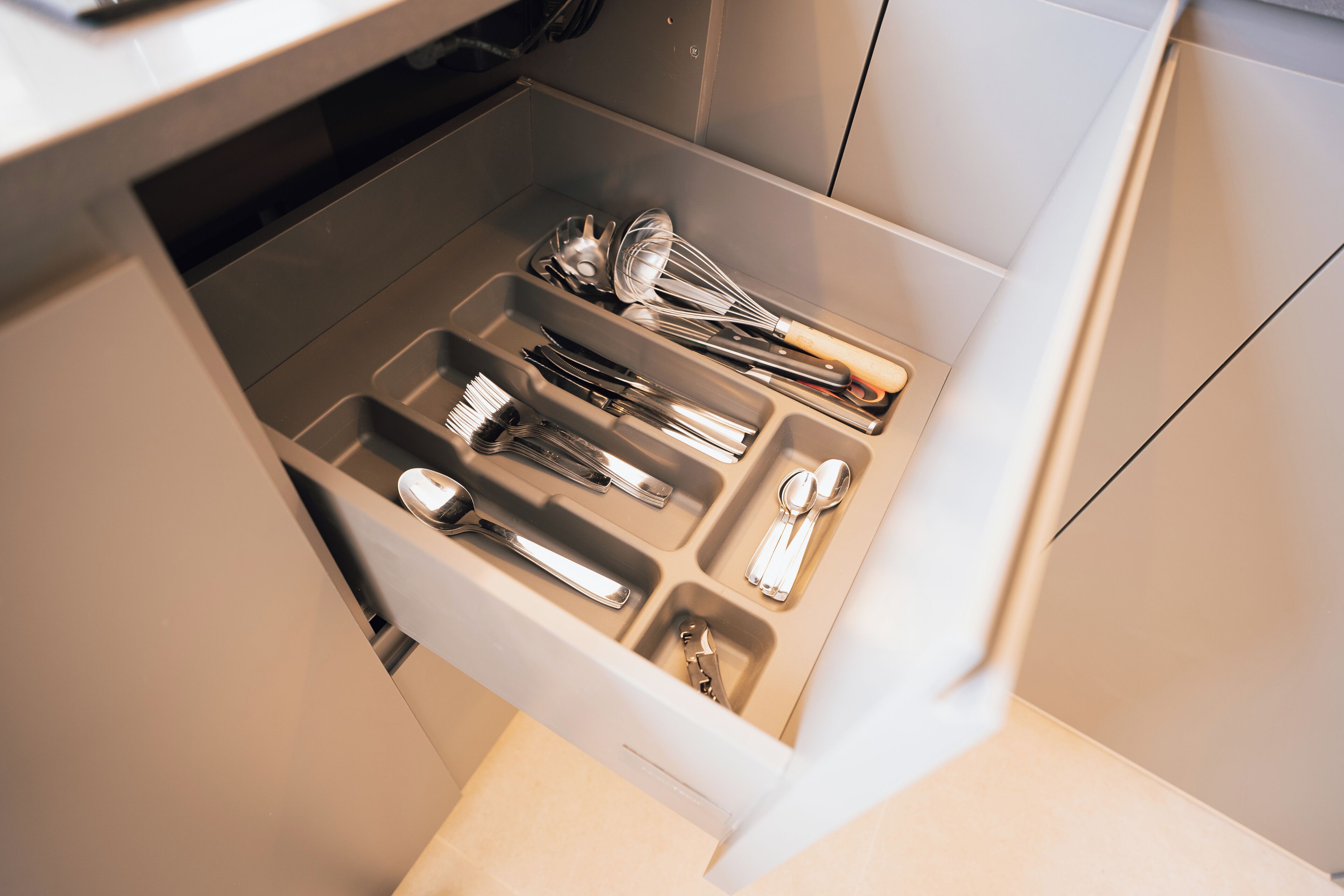 A drawer with various kitchen utensils including spoons, forks, and a whisk.