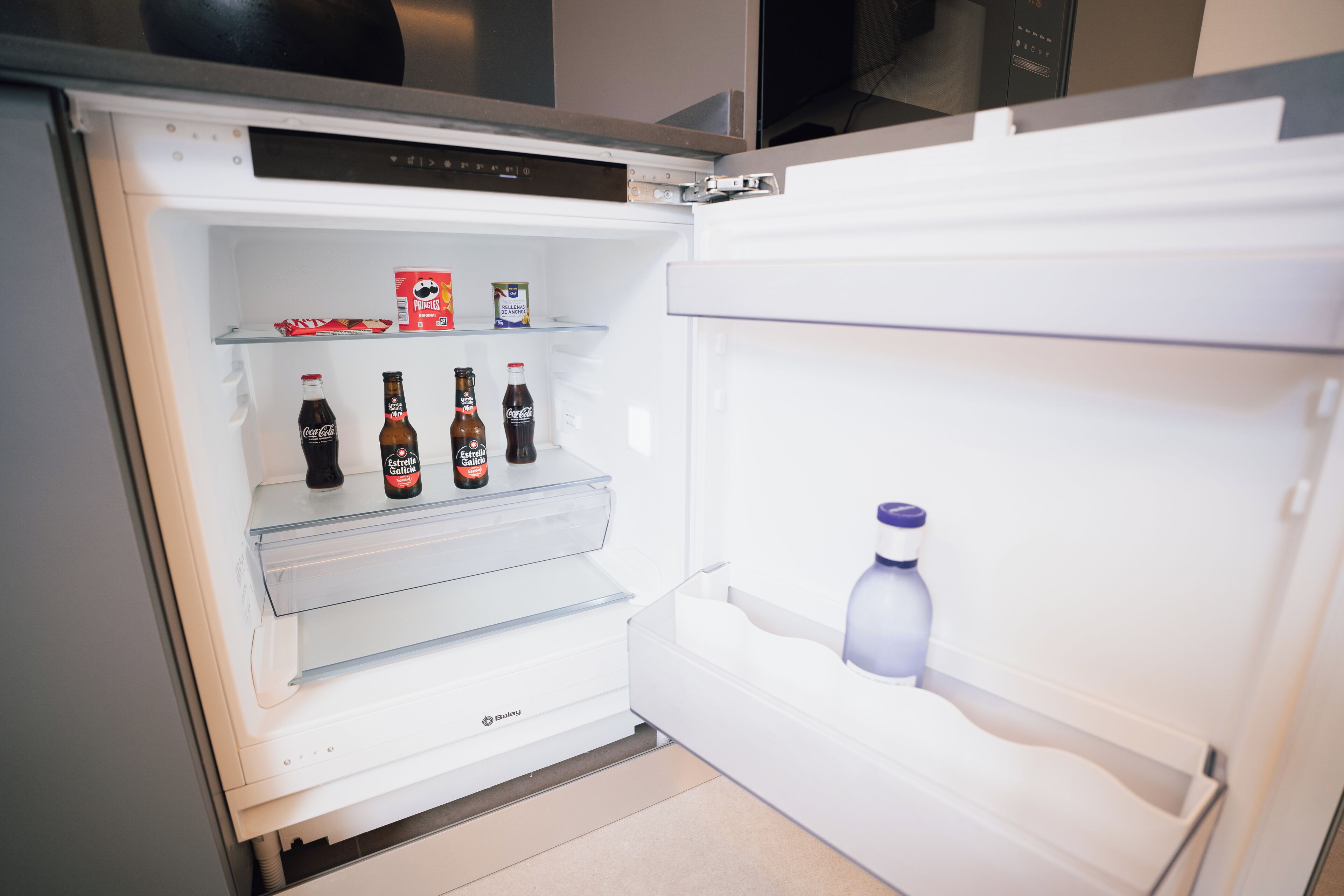 Un réfrigérateur ouvert, dont les étagères contiennent des boissons et des en-cas.