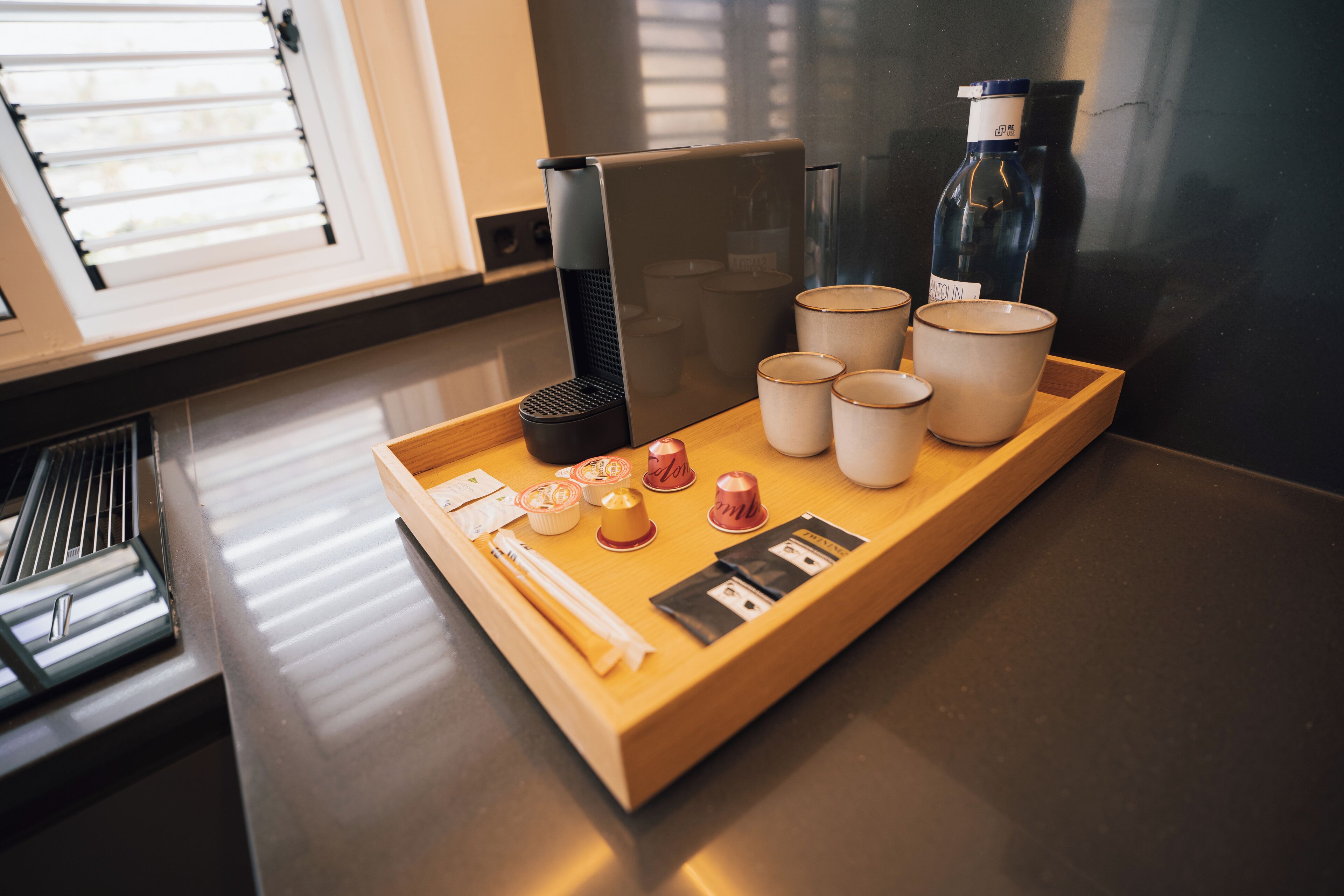 A tray with various items including cups, a bottle, and some small containers on a countertop.