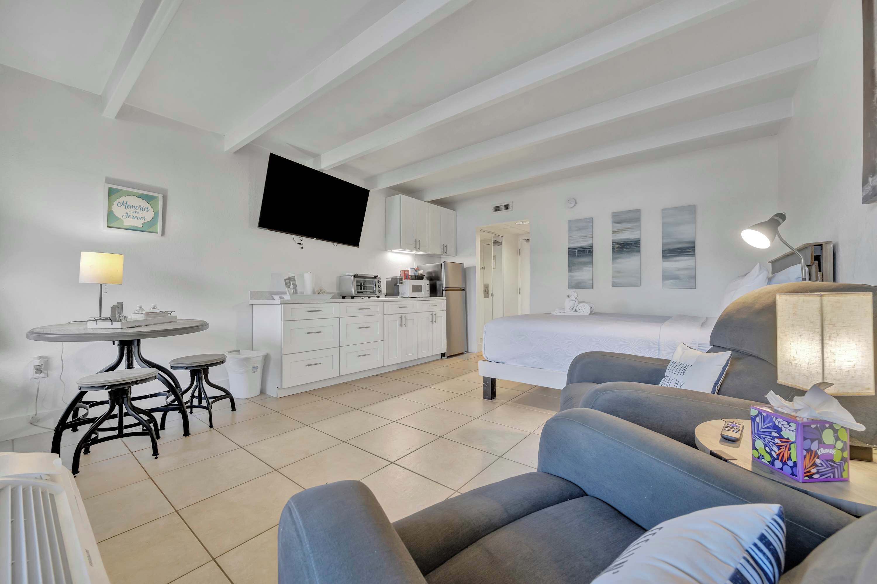 Une chambre d’hôtel moderne équipée d’un lit, d’un canapé, d’une table à manger avec des tabourets, d’un coin cuisine et d’un téléviseur à écran plat fixé au mur.