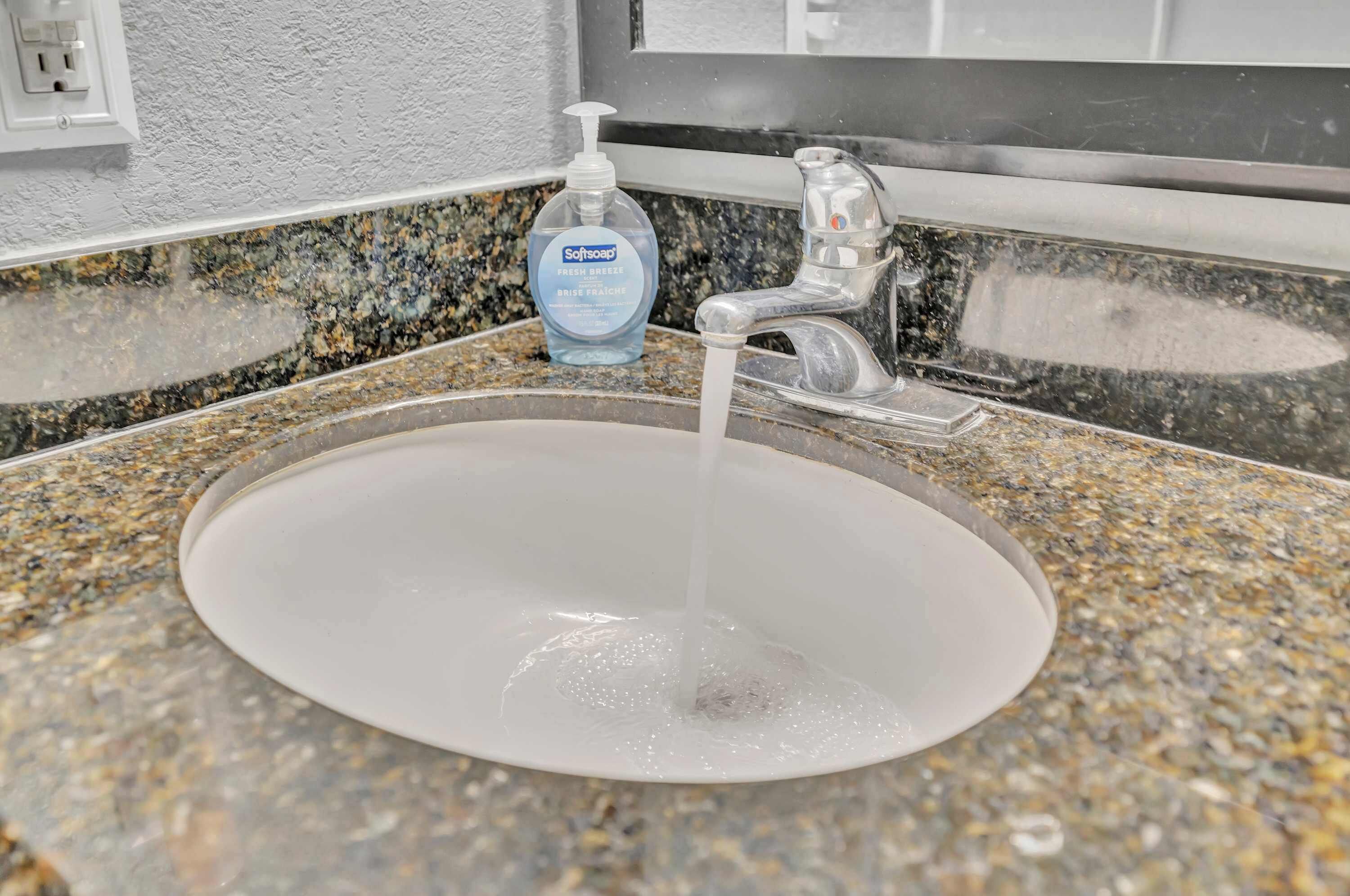 A bathroom sink with running water, a soap dispenser, and a granite countertop.