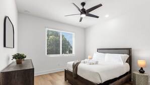 Une chambre à coucher comprenant un lit, un ventilateur de plafond, une table de chevet avec une lampe et une fenêtre avec des stores.
