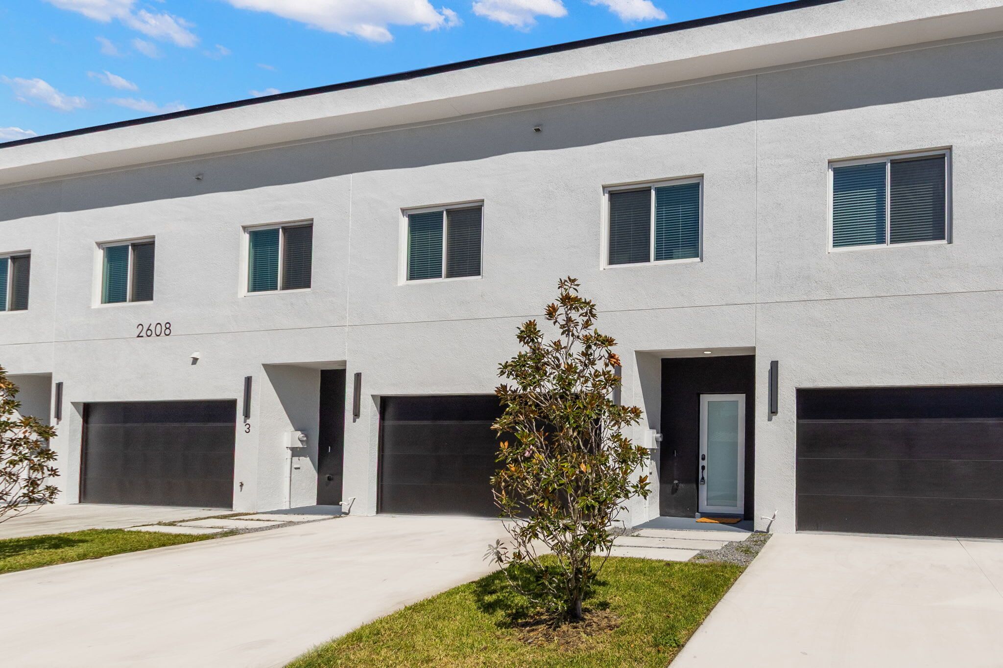 A modern building with a flat facade, numbered 2608, featuring multiple garage doors and a small tree in the foreground.