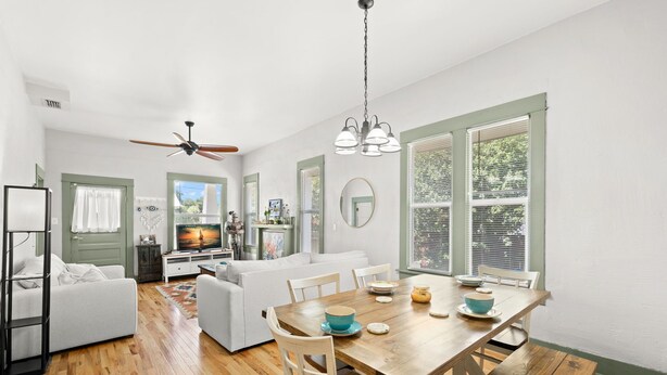 A modern living room with a dining area, wooden flooring, and large windows with green shutters. - NEW Lakeland Landing Cute Bungalow by Downtown (Lakeland)