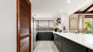 Una cocina moderna con una isla grande, armarios oscuros y vistas a una zona residencial.