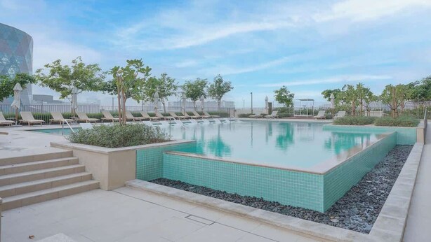 A swimming pool with lounge chairs and steps leading into it, surrounded by greenery.