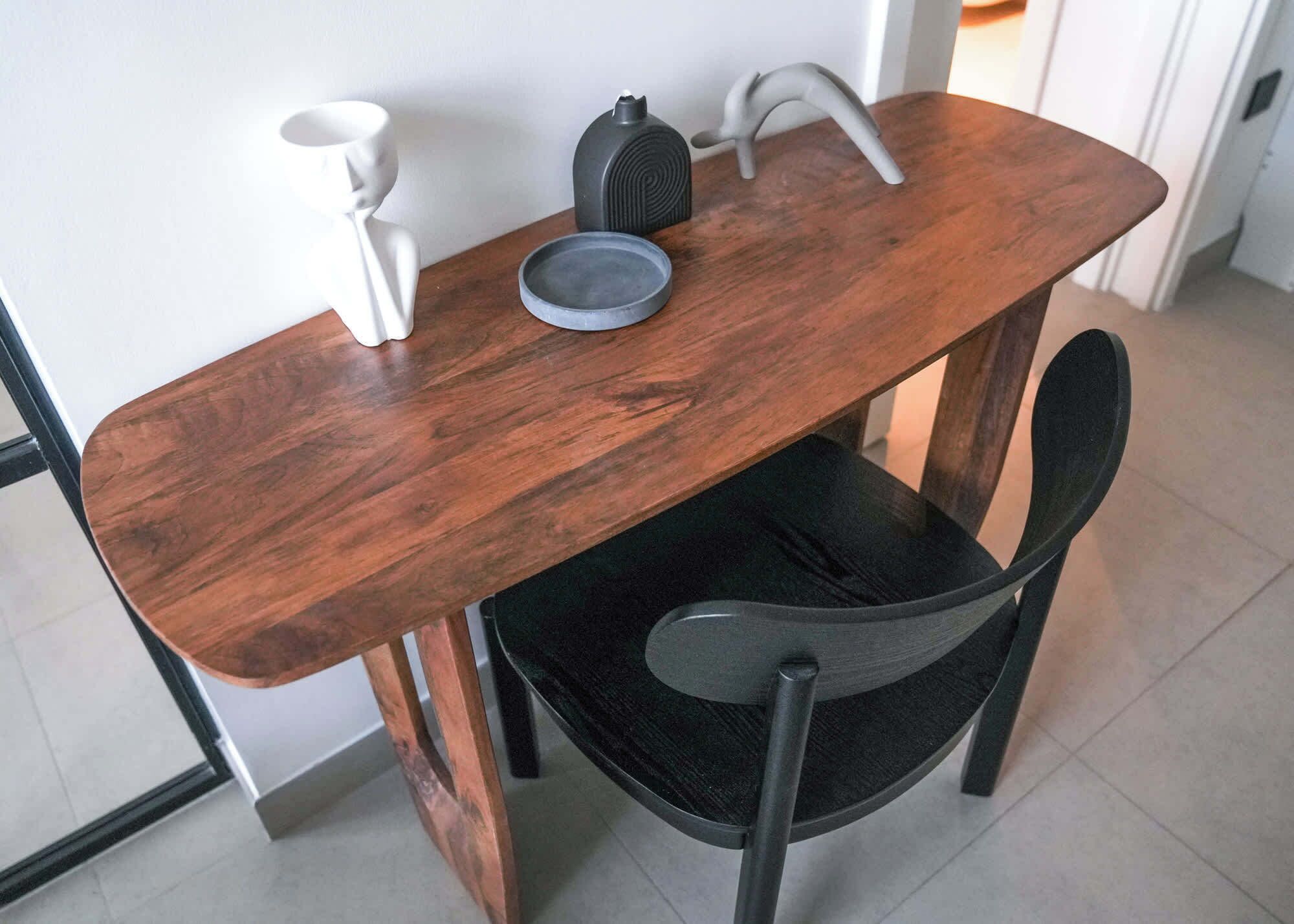 A wooden dining table with a black chair, a white vase, and a grey bowl.