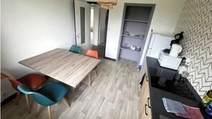 A compact kitchen with a wooden table, colorful chairs, a hanging light fixture, and a microwave on a counter. - Chill & relax (Limoges)