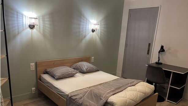 A bedroom with a wooden bed, two wall-mounted lights, a desk with a chair, and a door. - Chill & relax (Limoges)